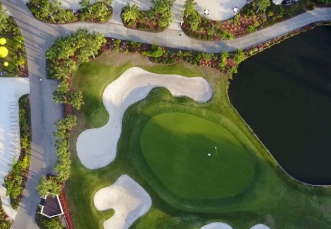 Aerial view of a golf course with a sand bunker, green, and a swimming pool nearby.