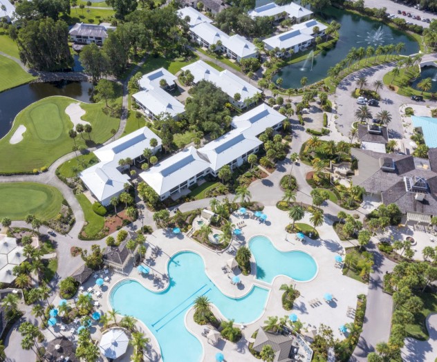 Aerial view of a resort with pools, buildings, and green areas.