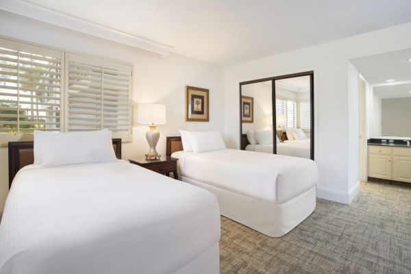 A clean, well-lit hotel room with two beds, nightstands, lamps, and a full-length mirror.