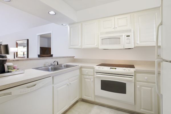 A clean, white kitchen with cabinets, microwave, stove, and sink.
