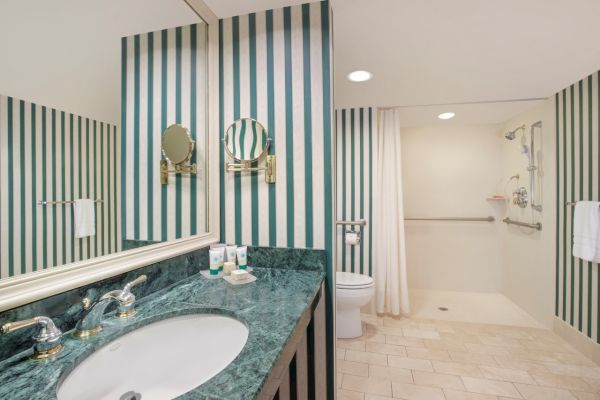 A bathroom with striped walls, a mirror, sink, and a visible shower area.