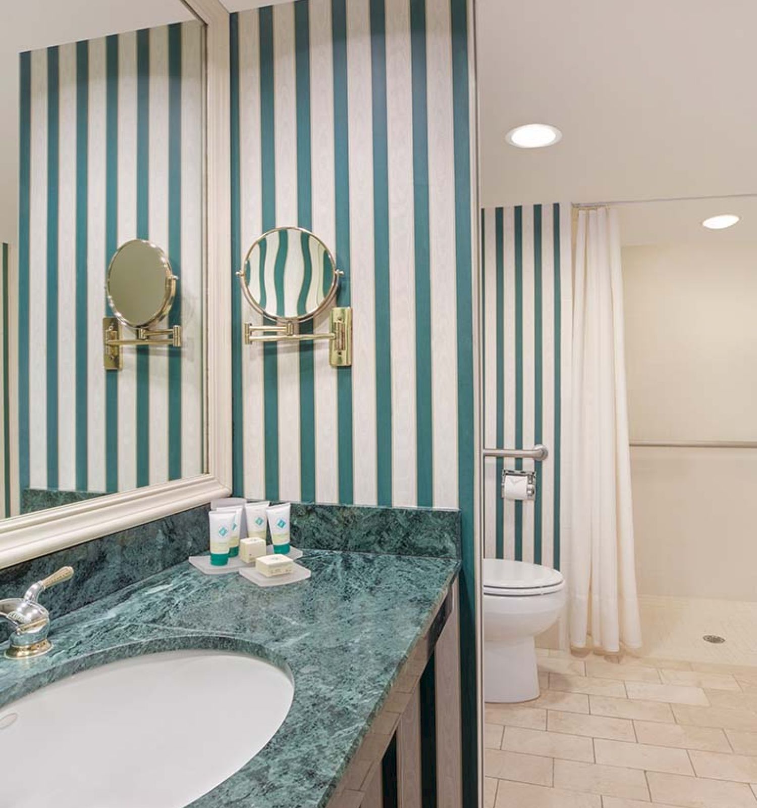 A bathroom with striped walls, sink, mirror, toiletries, and a glimpse of the shower curtain.