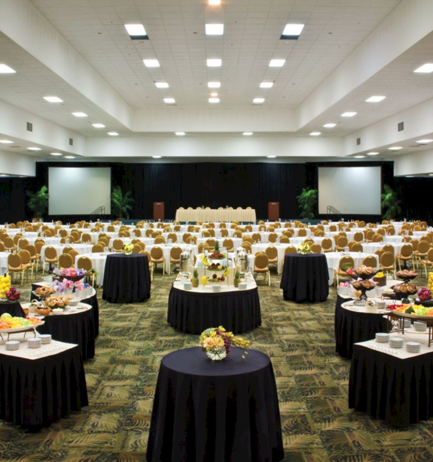 The image shows a large conference room set up with tables, chairs, and food stations, likely for a meeting or event.