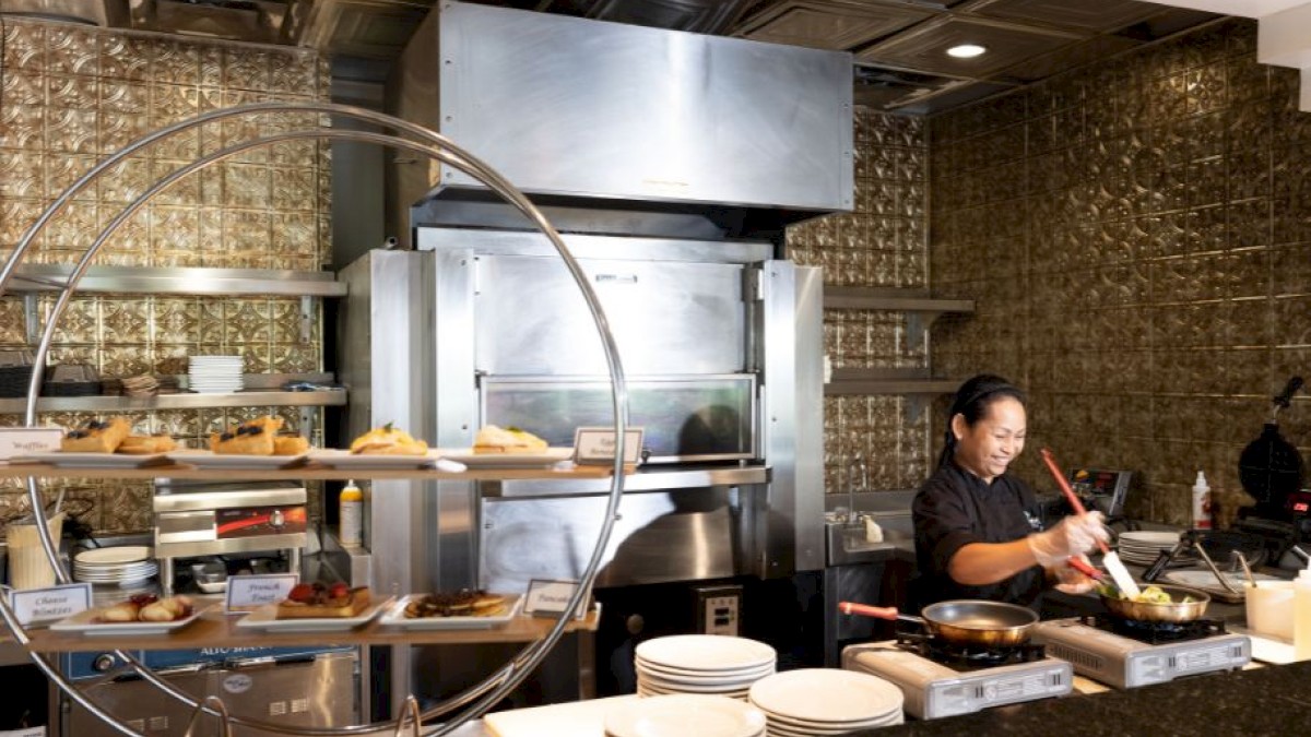 A chef is working in a modern kitchen, with various dishes displayed on round shelves and a stainless steel stove and oven in the background.