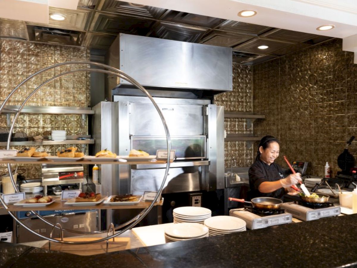 A chef is working in a modern kitchen, with various dishes displayed on round shelves and a stainless steel stove and oven in the background.