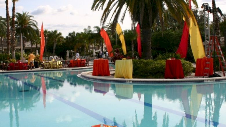 A poolside setup with tables covered in red cloth, a palm tree in the background, and colorful flags and decorations.