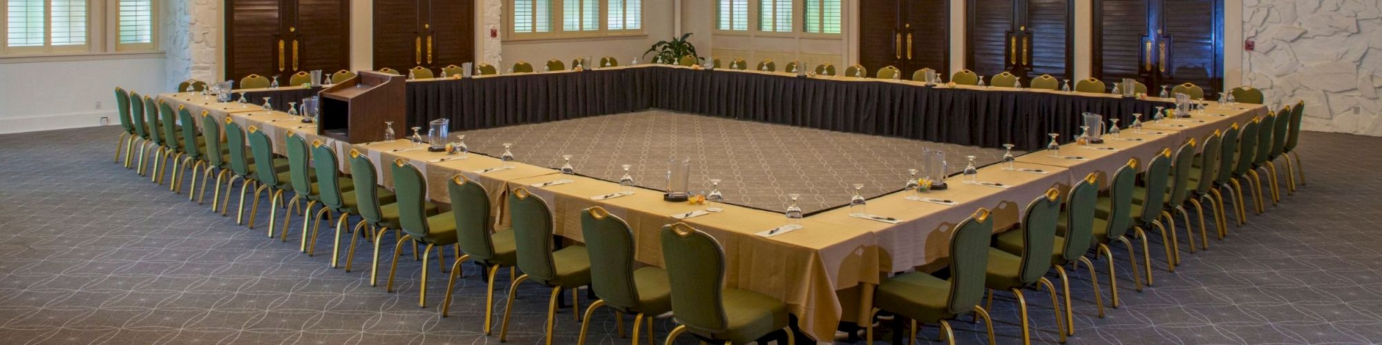 The image shows a large conference room set up with a U-shaped arrangement of tables and green chairs, ready for a meeting or event.