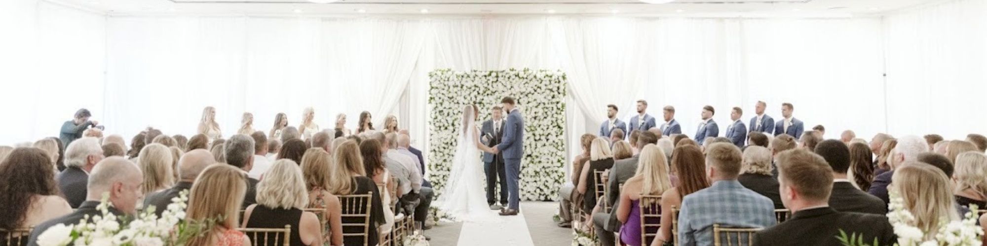 A wedding ceremony with the couple at the altar, bridesmaids and groomsmen beside them, and guests seated in rows watching.
