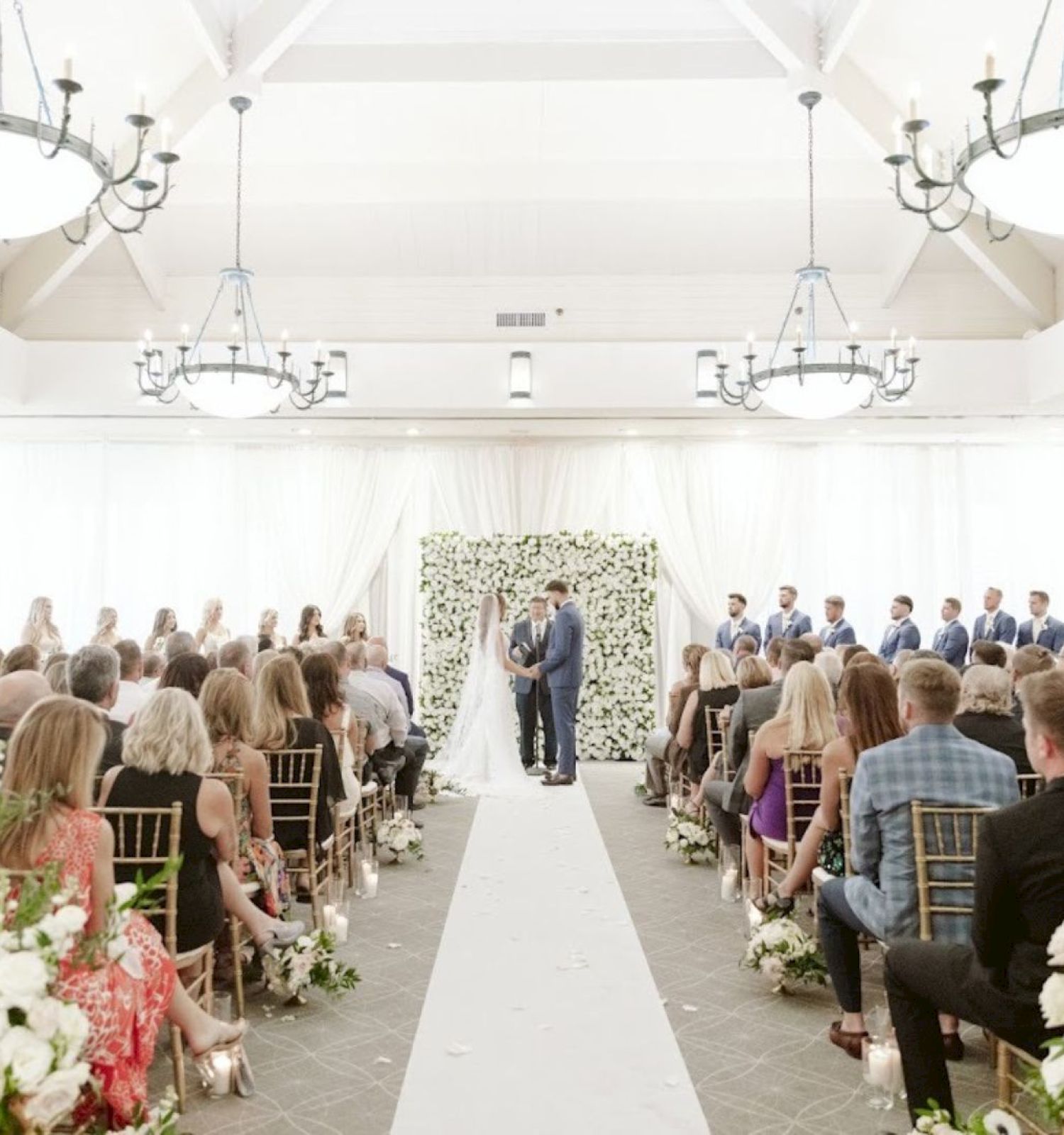 A wedding ceremony with a couple at the altar, bridesmaids and groomsmen on either side, and guests seated facing forward.