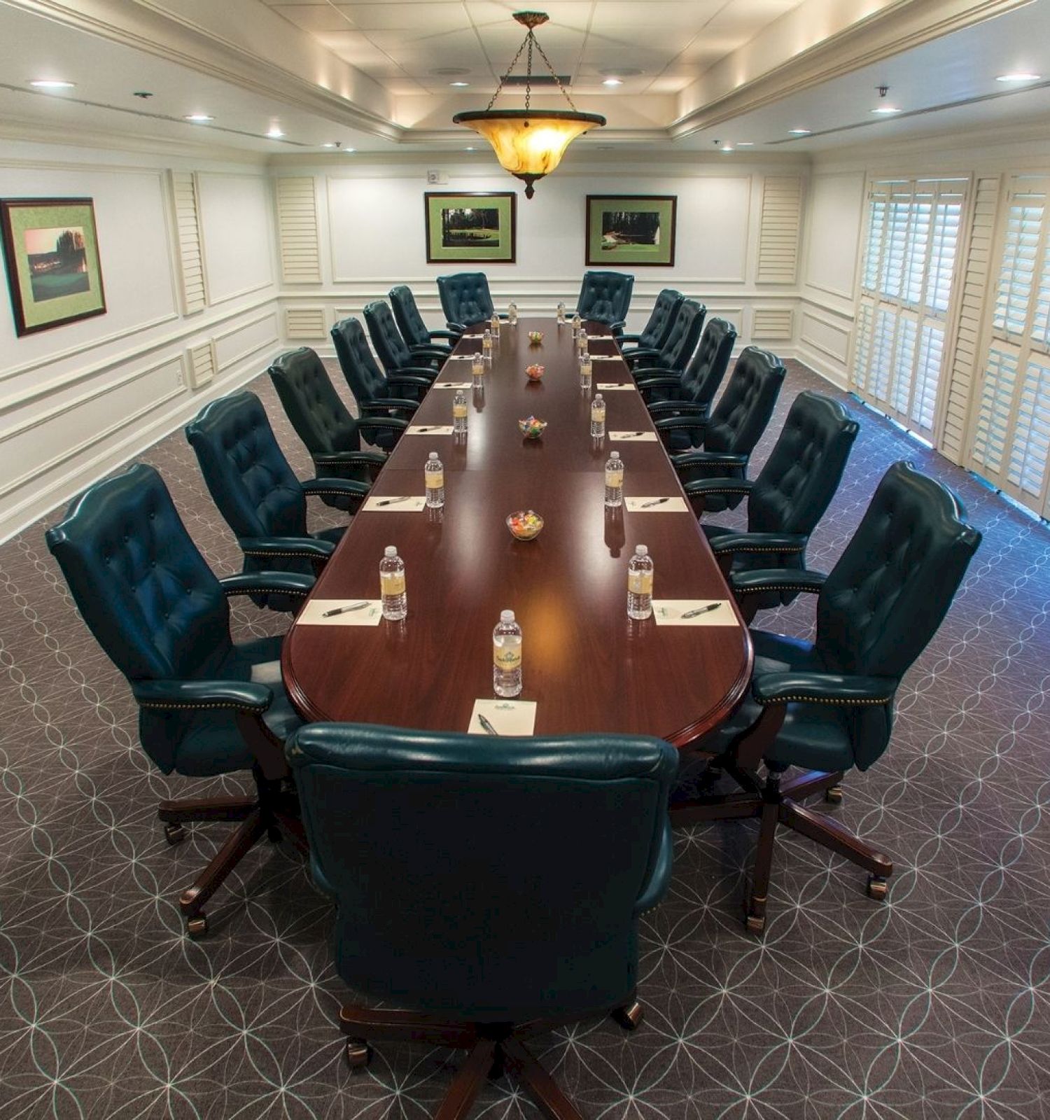 A large conference room with a long table, surrounded by green chairs, water bottles, and notepads set for a meeting. Art decorates the walls.