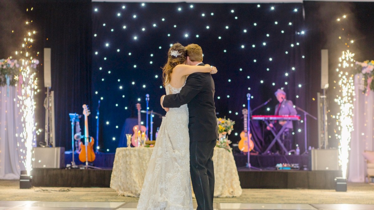 A couple is dancing on a stage with instruments and a keyboardist in the background, surrounded by decorative lights and sparklers.