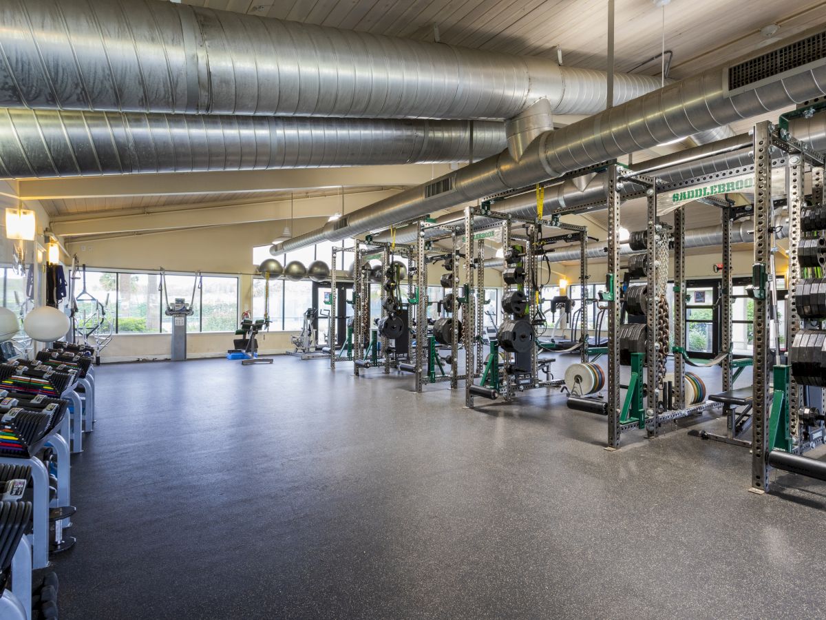 This image shows a spacious, modern gym with various fitness equipment, including weights and exercise machines, under industrial-style ducting.