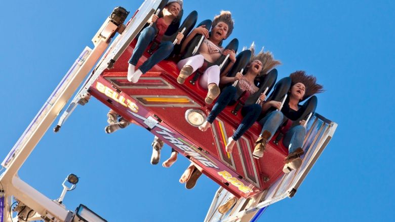People are on a thrill ride, hanging upside down with expressions of excitement and fear against a clear blue sky.