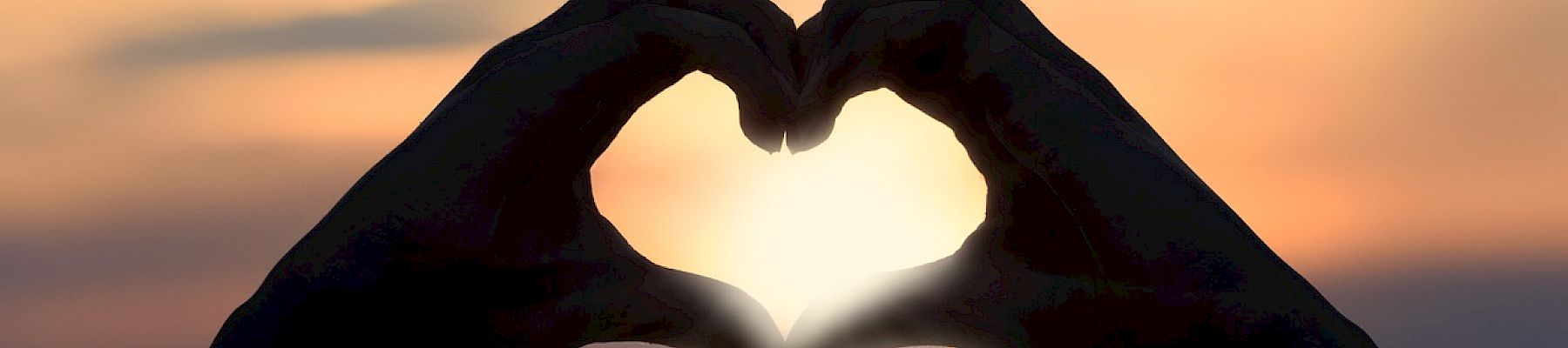 Silhouetted hands forming a heart shape against a sunset or sunrise background, with light shining through the heart opening.