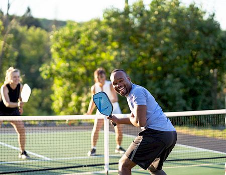 A group of people playing pickleball on an outdoor court, with three women and one man having fun and holding paddles, ending the sentence.