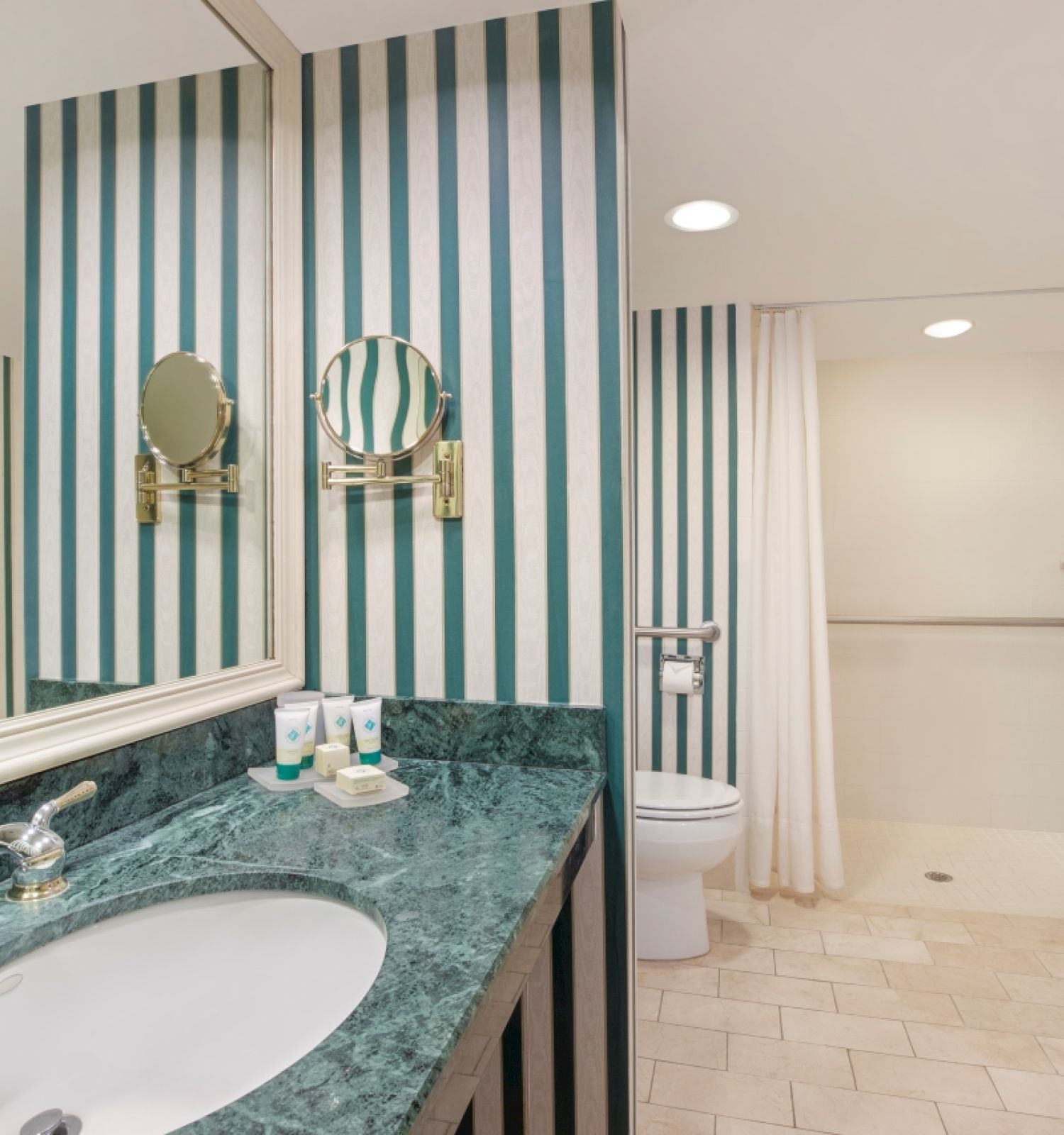 A bathroom with striped wallpaper, mirror, sink, and a visible shower area.