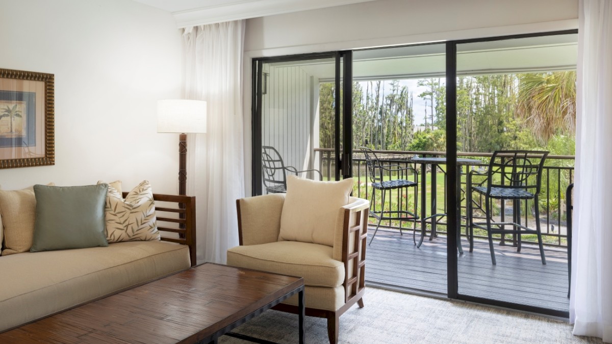 A cozy room with a sofa, chairs, a table, and a balcony overlooking greenery.