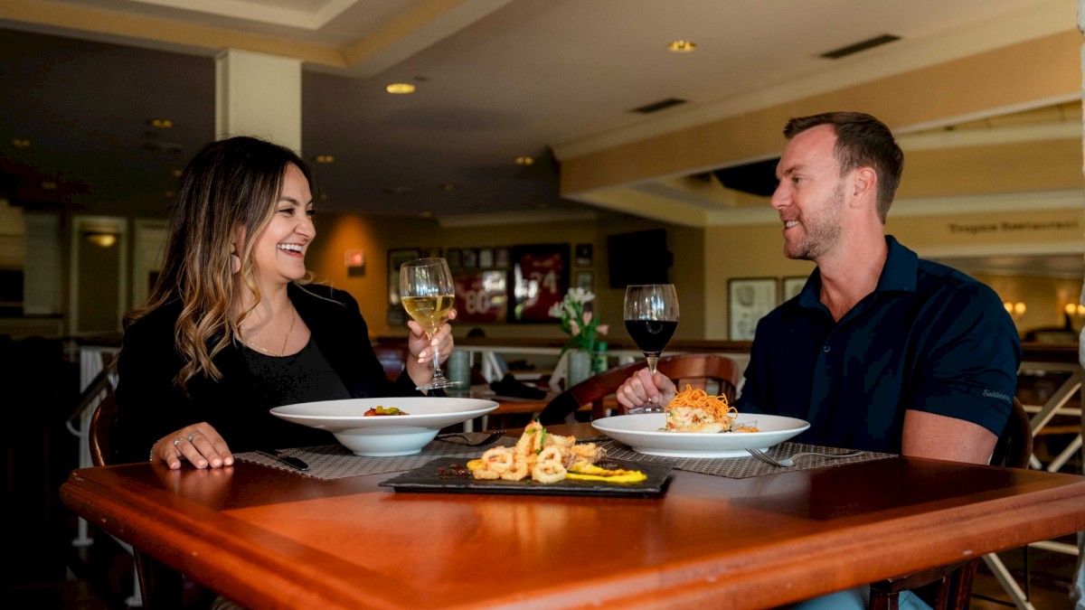 A couple enjoys a meal at a restaurant, sharing smiles and holding wine glasses.