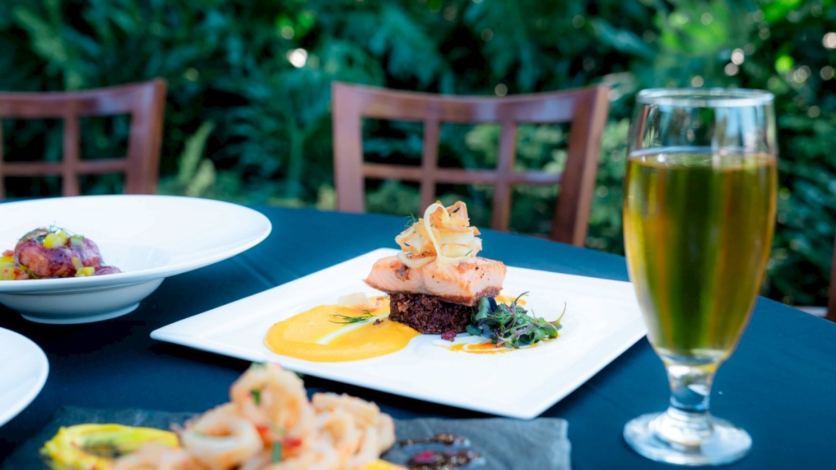 A table with a gourmet seafood dish, a glass of beer, and other dishes in an outdoor setting.