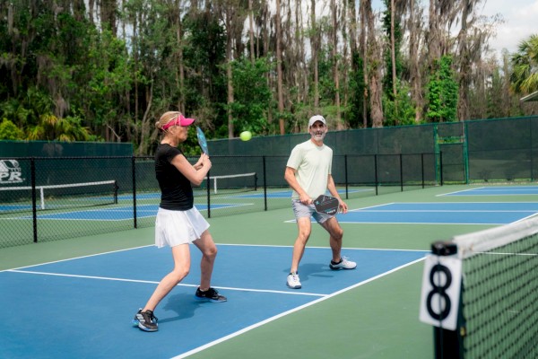 Two people are playing tennis on a blue court.
