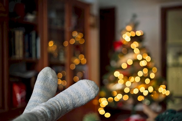 Cozy socks in the foreground with a softly focused, lit Christmas tree in the background, creating a warm holiday atmosphere.