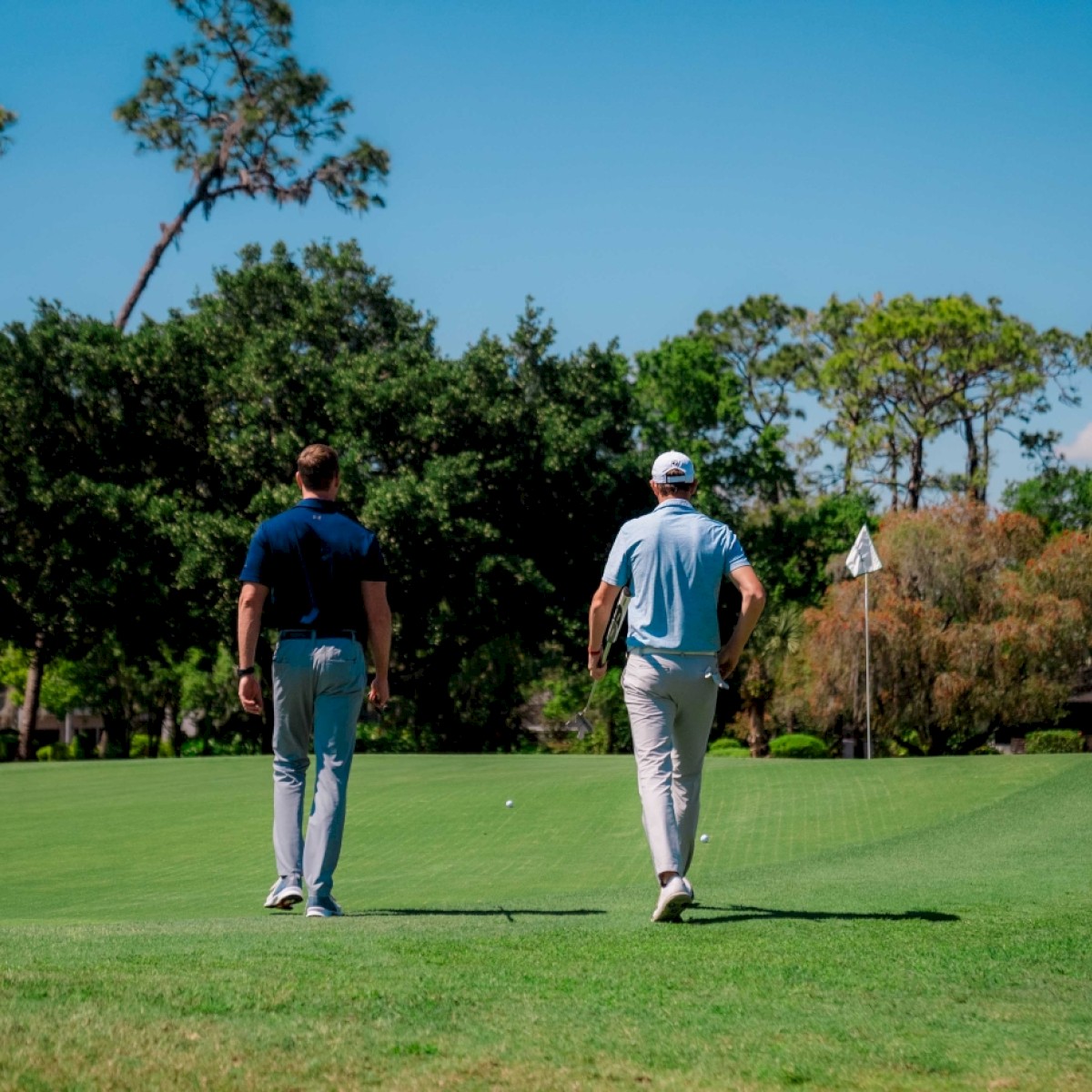 Two people walking on a golf course with clubs.