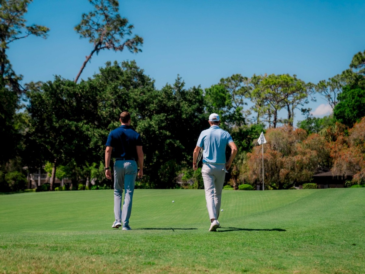 Two people walking on a golf course with clubs.