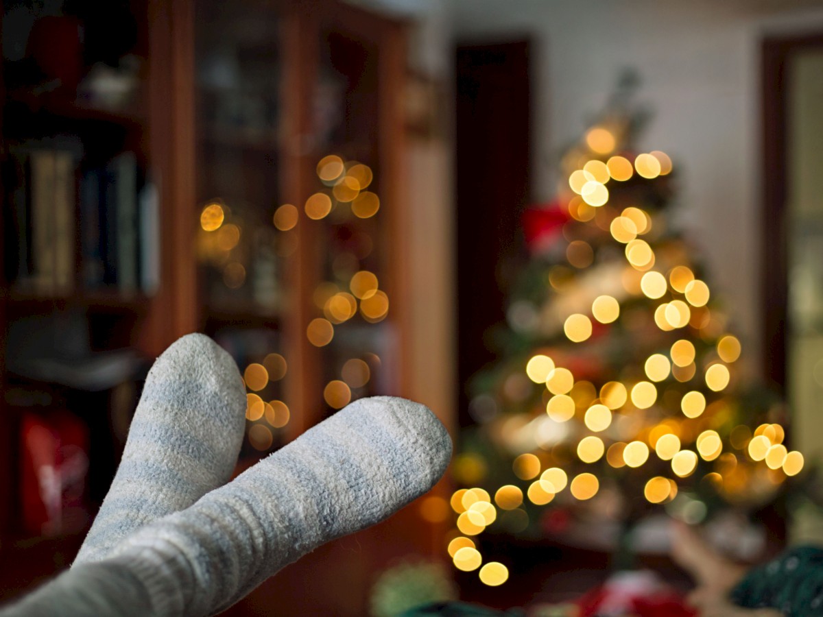 Cozy socks in the foreground with a blurred Christmas tree and warm lights in the background, creating a festive atmosphere.