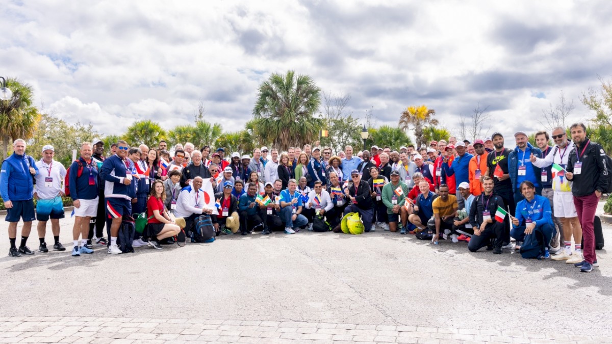 A large group of people posing for a photo outdoors, with trees and a partly cloudy sky in the background.