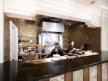 A chef is cooking in a stylish kitchen with a black countertop. The kitchen features stainless steel appliances and decorative tile walls.