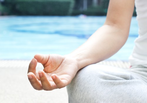 A person is meditating with a hand gesture called a mudra near a pool.
