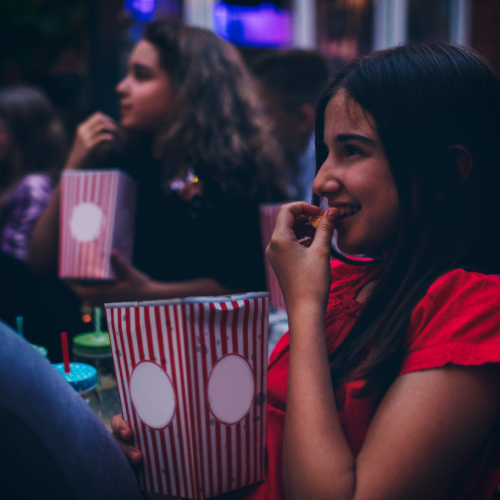 A person is smiling, holding popcorn, with others in the background.