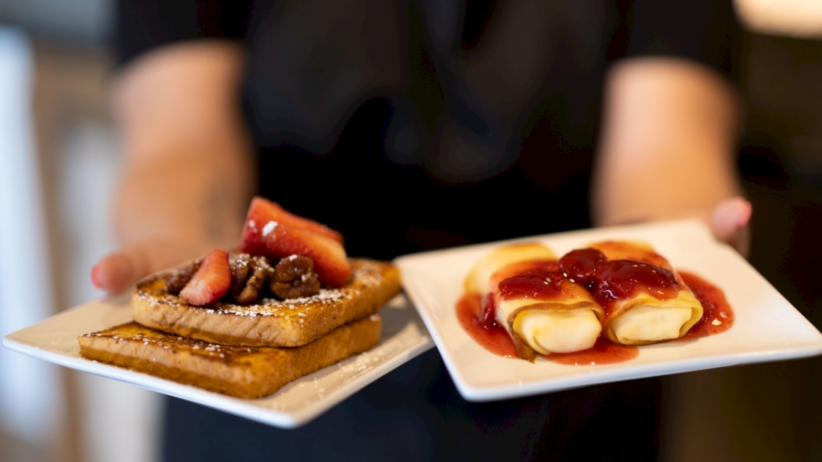 A person holding two plates of desserts, one with fruit tarts, one with creamy pastries.