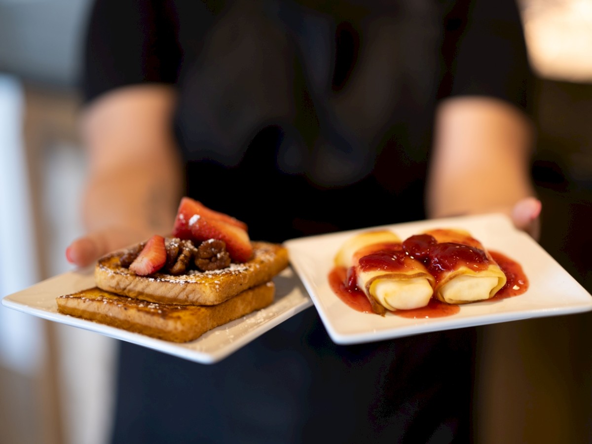 A person holding two plates of desserts, one with fruit tarts, one with creamy pastries.