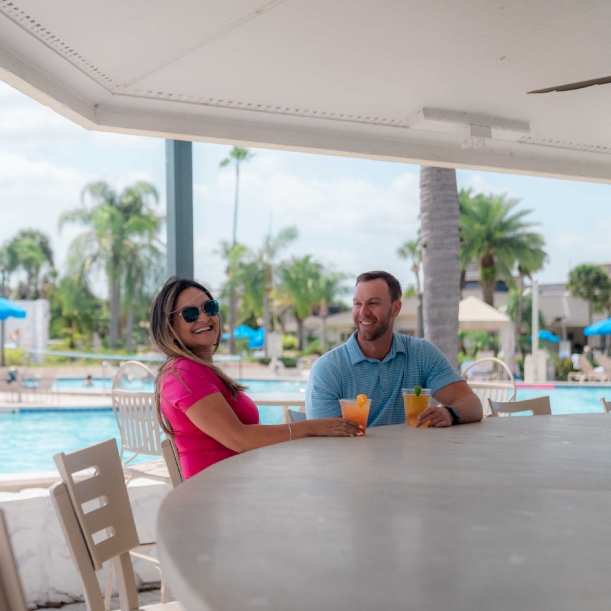 Two people are sitting at a bar by a pool, enjoying drinks and conversation.