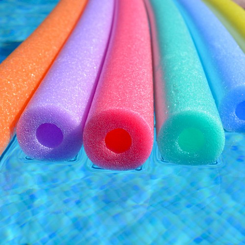 The image shows six colorful pool noodles floating on the surface of a swimming pool, half-submerged in the water.
