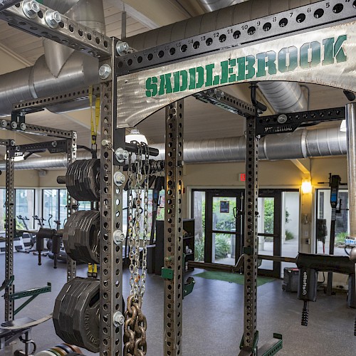 The image shows a well-equipped gym with various weightlifting and fitness equipment and the sign 