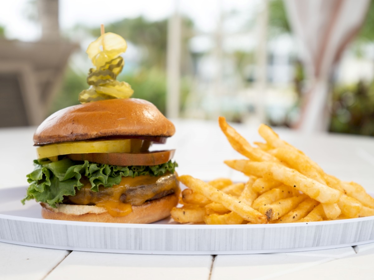 The image shows a delicious burger with lettuce, cheese, and pickles, accompanied by a side of crispy seasoned fries, served on a white plate.