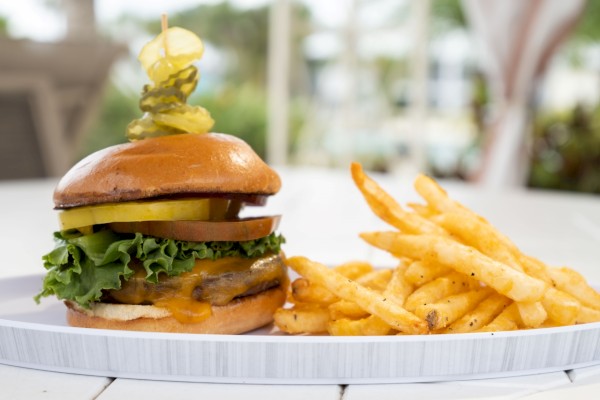 A delicious burger with melted cheese, lettuce, tomato, and pickles on a toothpick, served with a side of seasoned French fries.