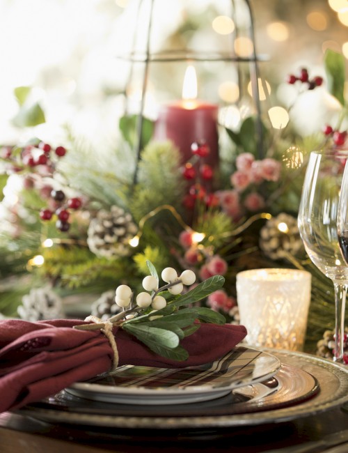 A festive table setting with wine glasses, candles, and holiday decorations including berries and pine cones, creating a warm and elegant atmosphere.