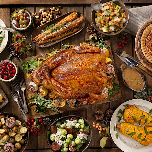 The image shows a Thanksgiving feast with a roasted turkey, stuffing, pie, cornbread, vegetables, mashed potatoes, cranberries, and assorted side dishes.