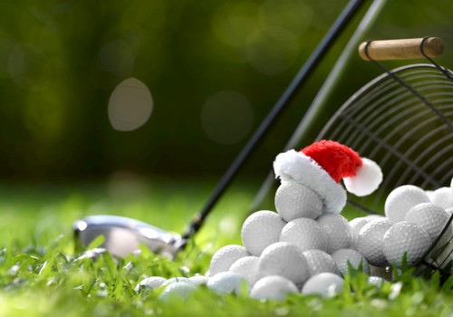 A pile of golf balls, one with a Santa hat, next to a basket and golf club on grass.