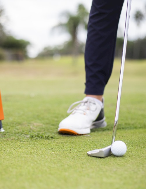 A golfer prepares to putt, next to an orange TrackMan device on a grassy field.