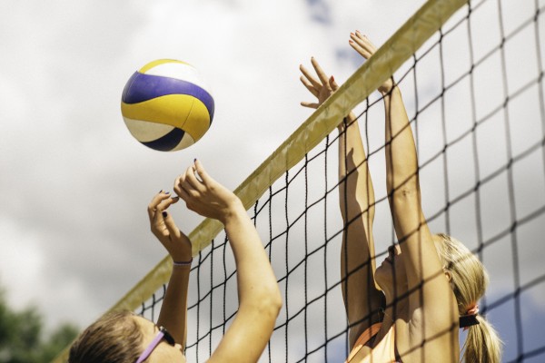 Two people are playing beach volleyball, with one spiking and the other blocking at the net on a sunny day.