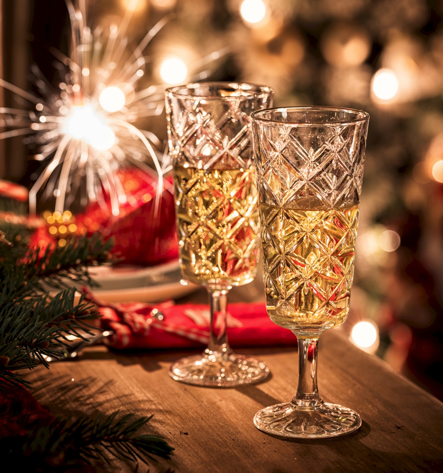 Two glasses of champagne on a table with a festive background, featuring warm lights and a sparkling decoration.