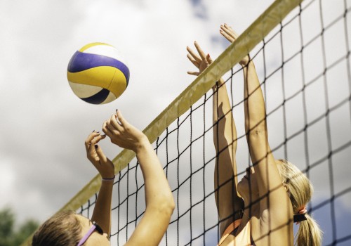 Two players at a volleyball net, one attempting to block a ball while the other prepares to spike it.