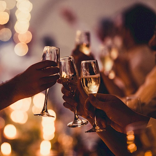 People are toasting with champagne glasses at a festive gathering, with warm lighting and blurred background creating a cozy ambiance.