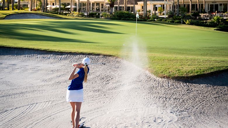 A golfer plays a shot from a sand bunker onto the green.