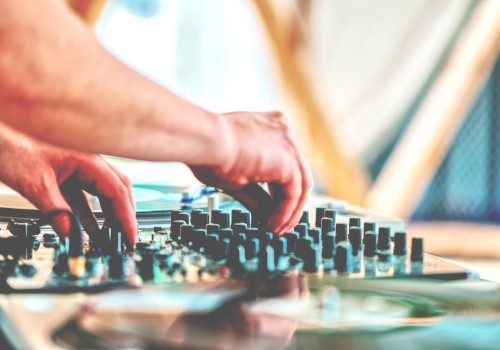 A person is adjusting controls on a DJ mixer, with hands focused on the knobs and sliders.