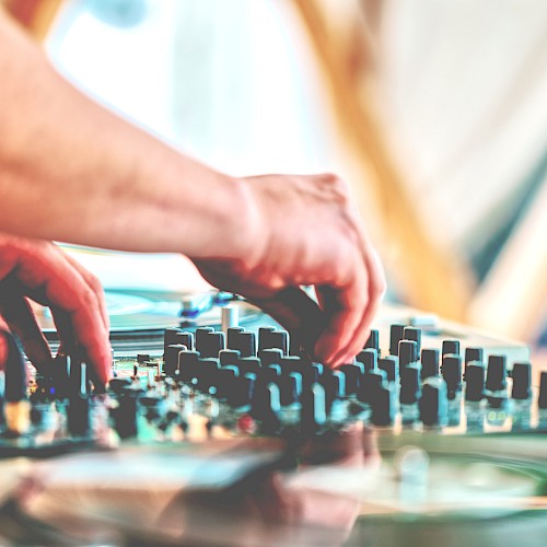 A person is adjusting controls on a DJ mixer, with hands focused on the knobs and sliders.